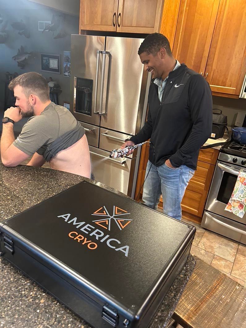Two men in a kitchen, one seated and one standing near a counter with an America Credit bag in the foreground.