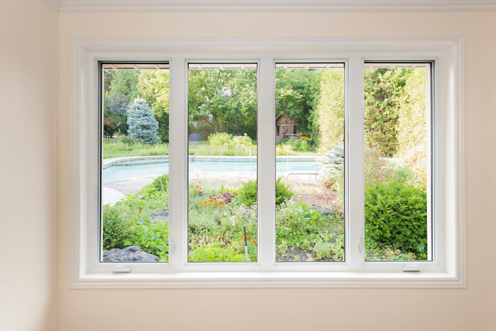 A white-framed, four-pane window overlooking a lush backyard garden with a swimming pool and trees.