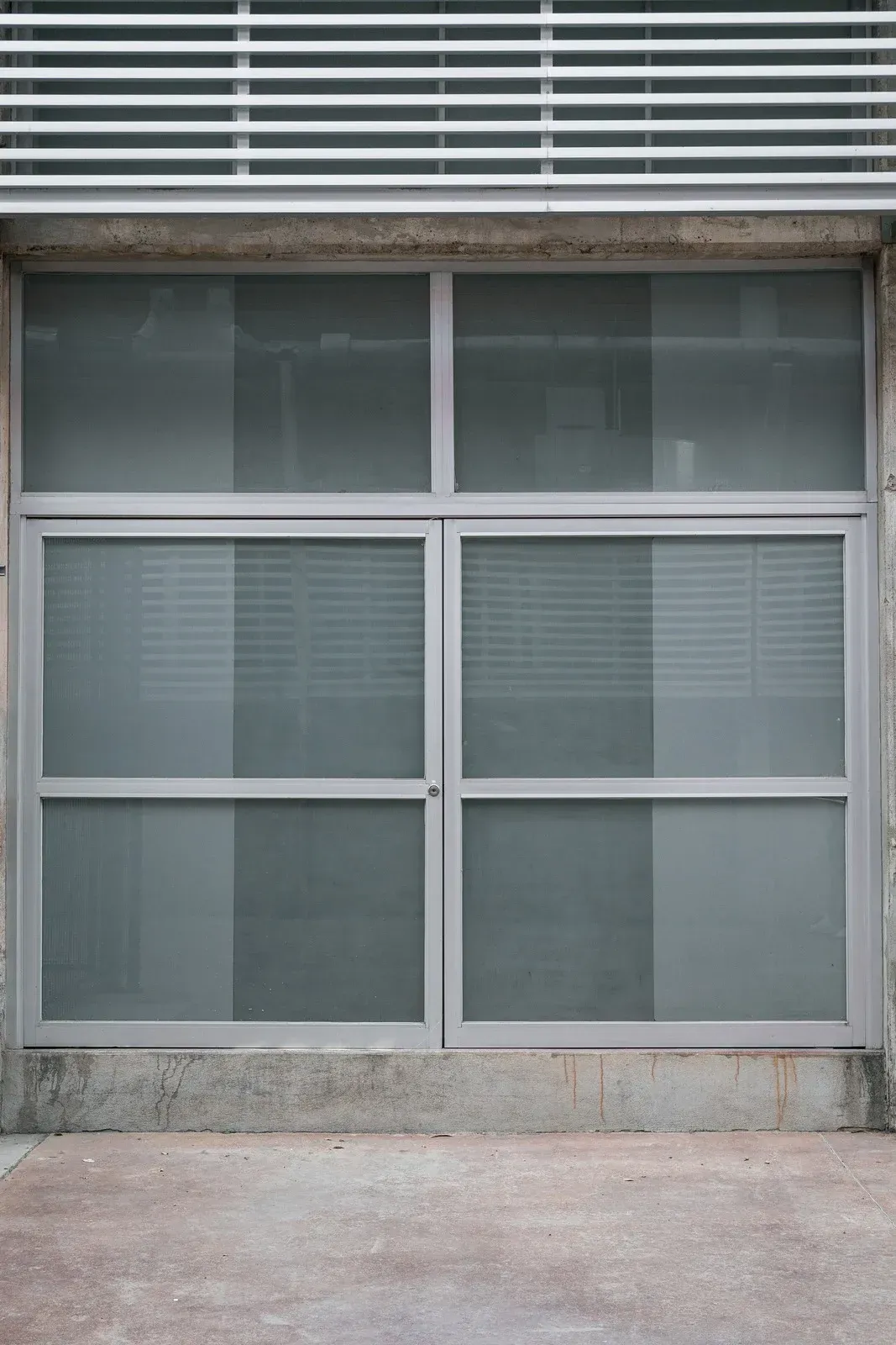 A rectangular storefront window with gray metal framing and frosted glass panes, situated above a concrete base.
