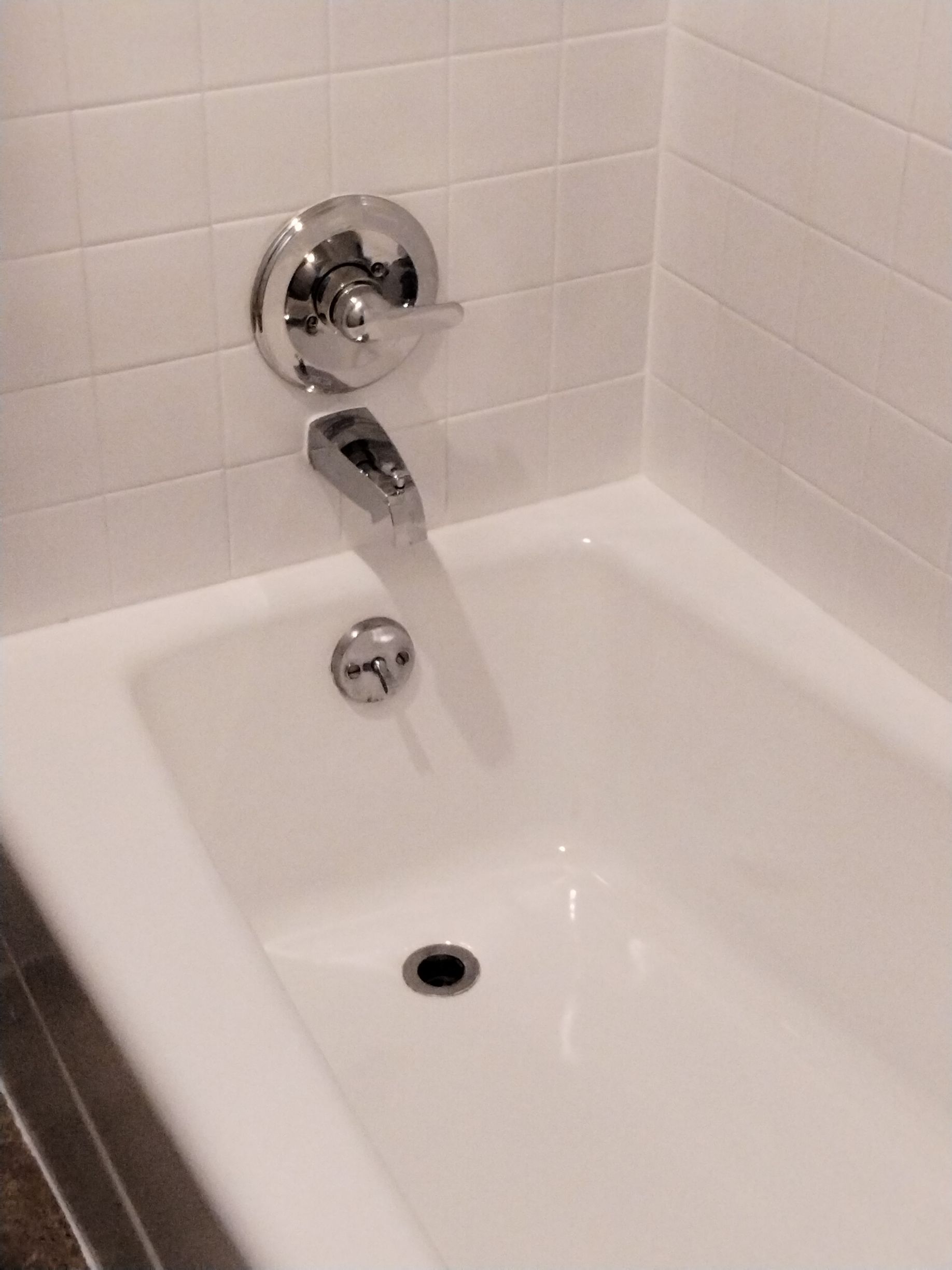 White bathtub with chrome faucet and drain, set against white tiled walls.