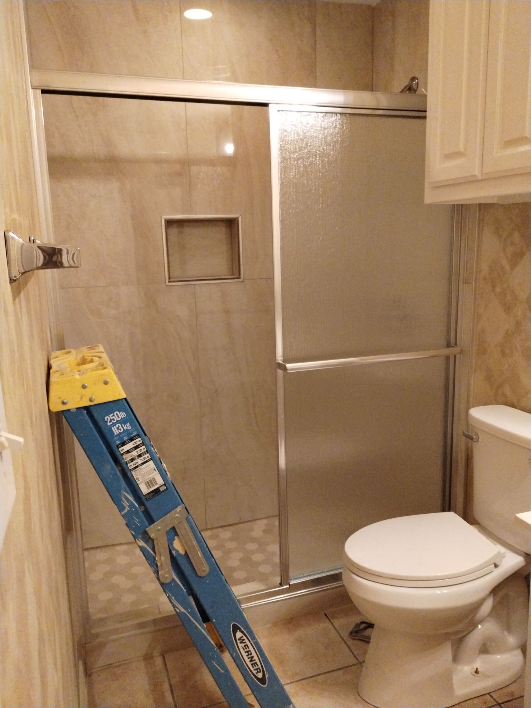 Small bathroom with a shower, toilet, cabinets, and a blue ladder.