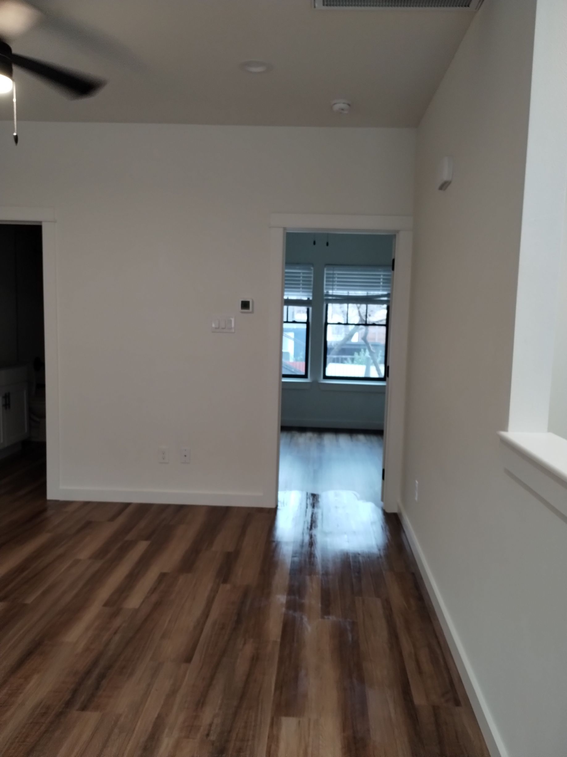 Interior view of room with wood flooring, an open doorway to another room with window.