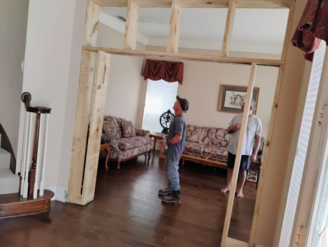 Two people, one child, in a room framed by new wood, looking into another room with furniture.