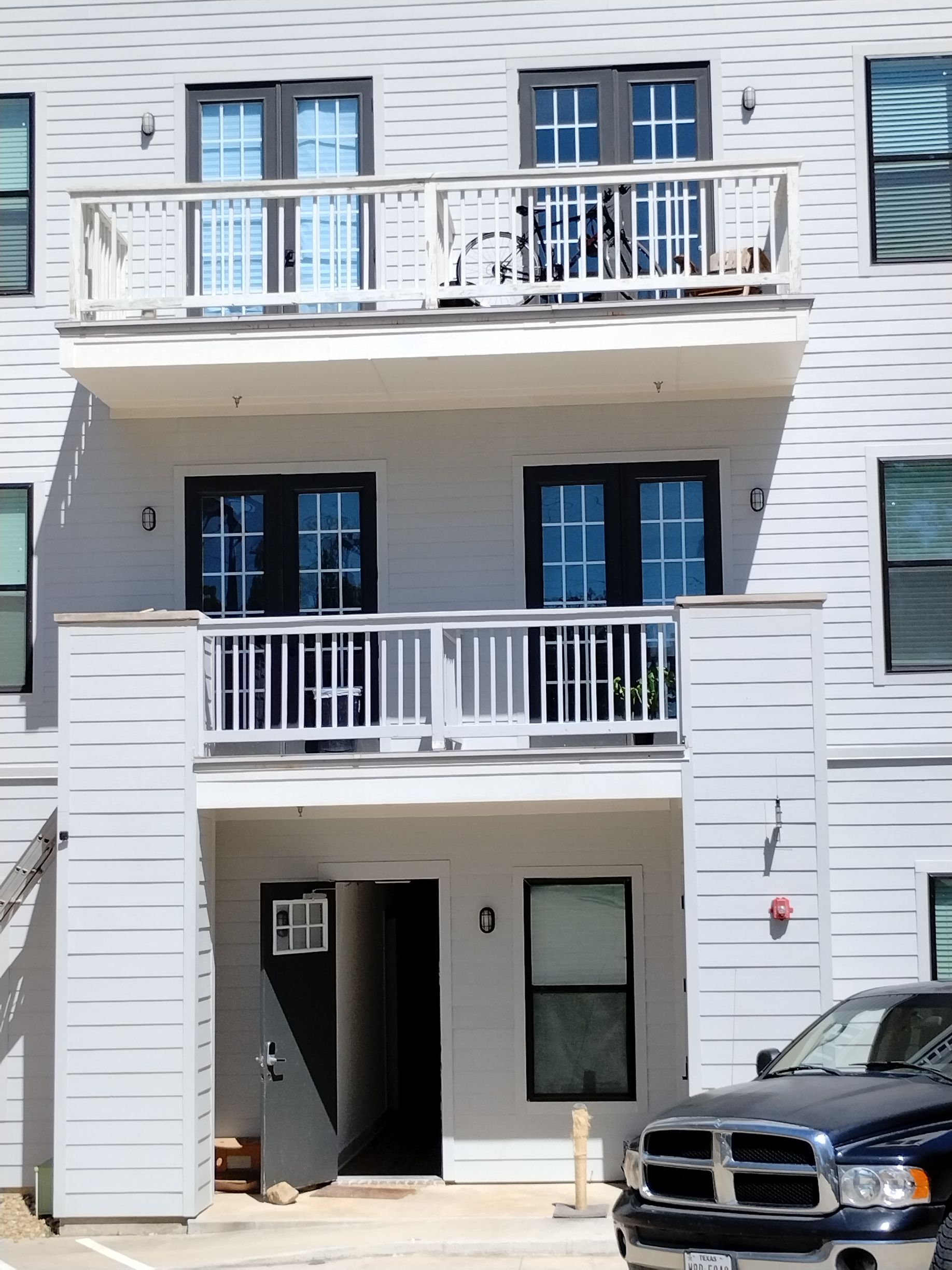 Gray apartment building with balconies and black framed doors/windows. A truck is parked in front.