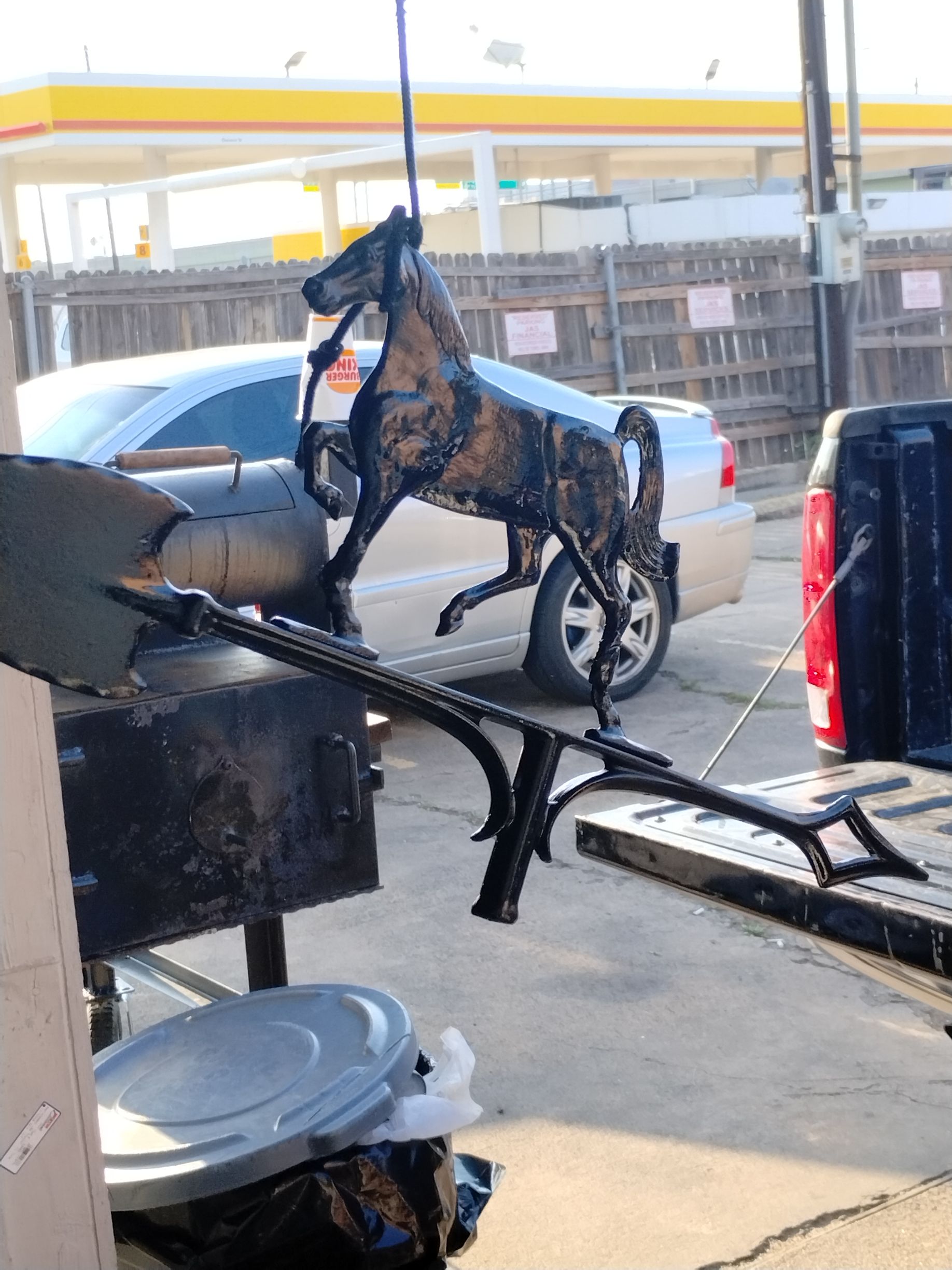 Metal horse statue suspended near a truck, ready to be transported. The scene is outdoors at a gas station.