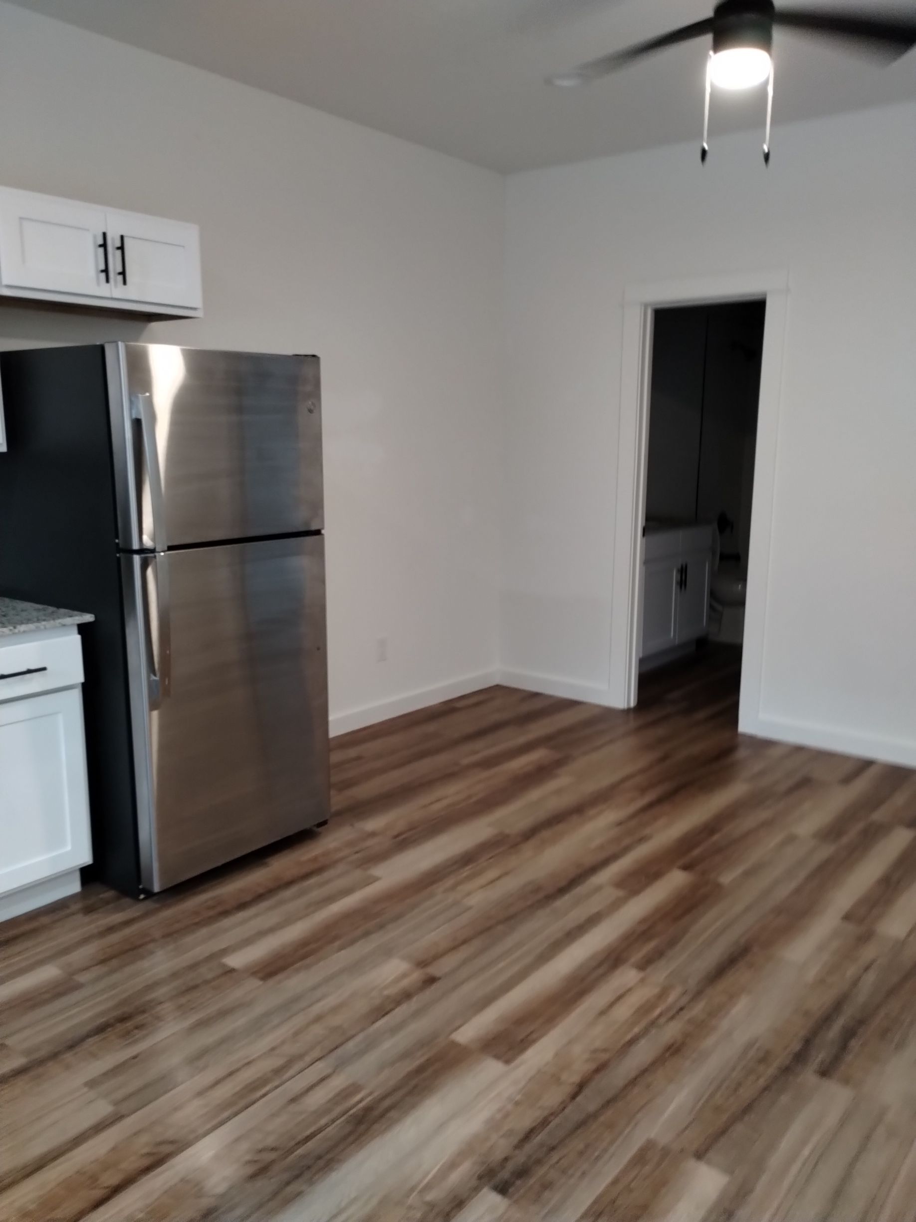 Stainless steel refrigerator in a kitchen with wood-look flooring, white walls, and a door to a bathroom.