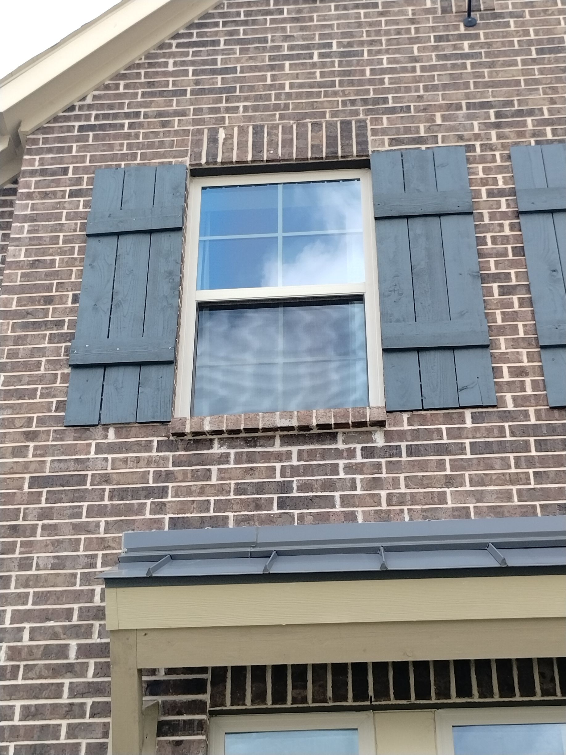 Brick home with a window flanked by blue shutters; a blue sky is reflected in the glass.