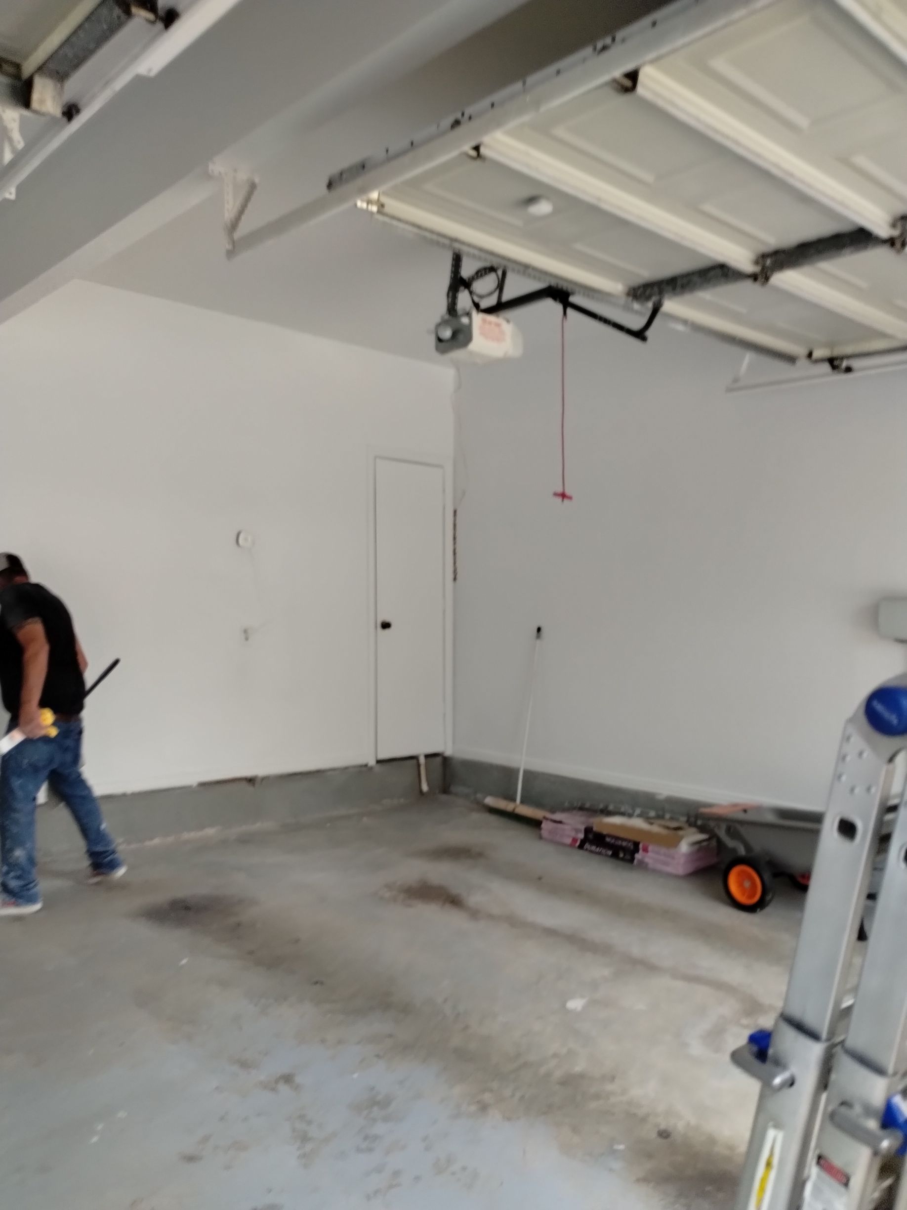 Man painting garage interior white, near door. Gray concrete floor, ceiling with garage door.
