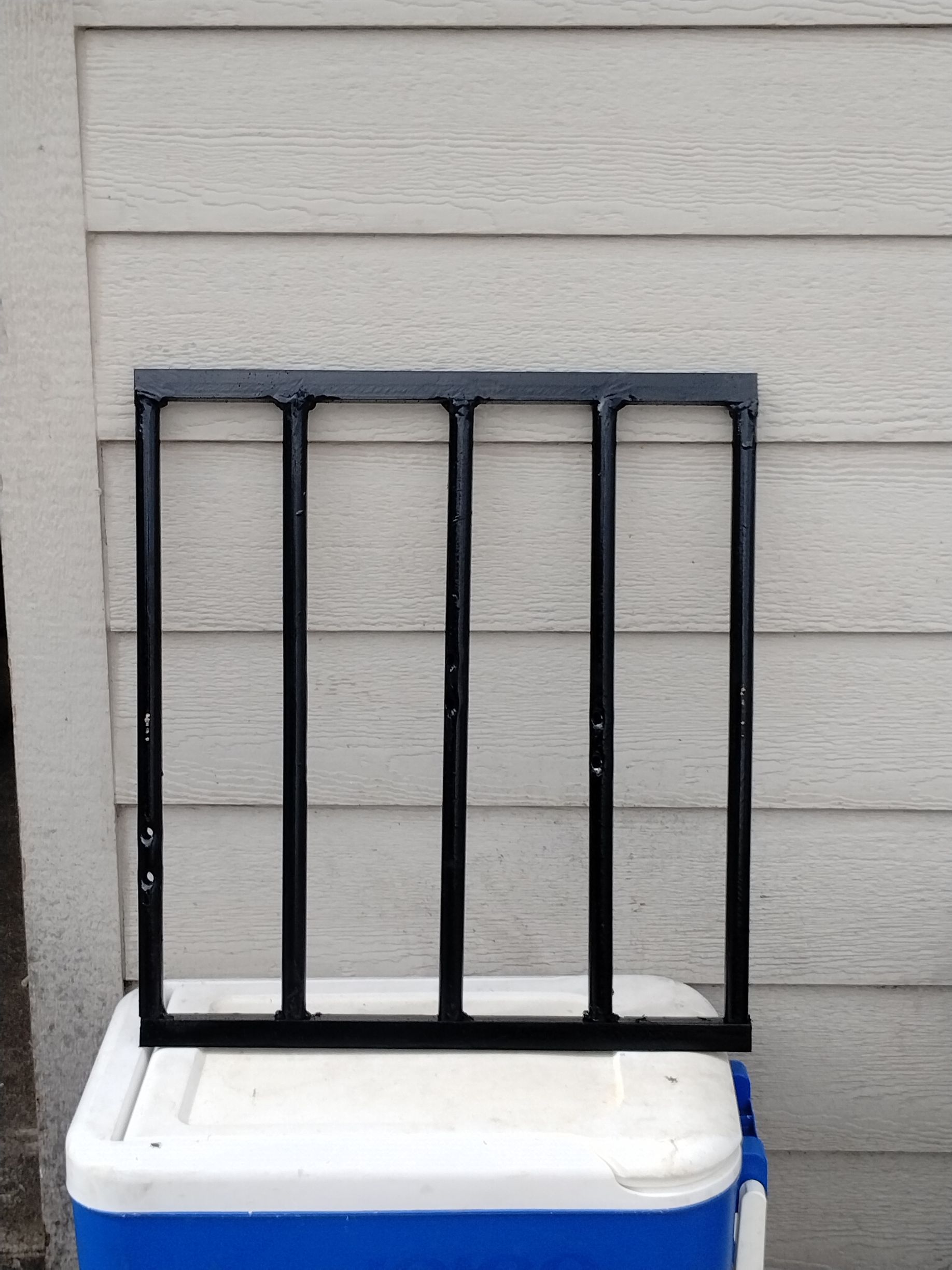 Black metal grate set atop a blue and white cooler, against a beige wall.