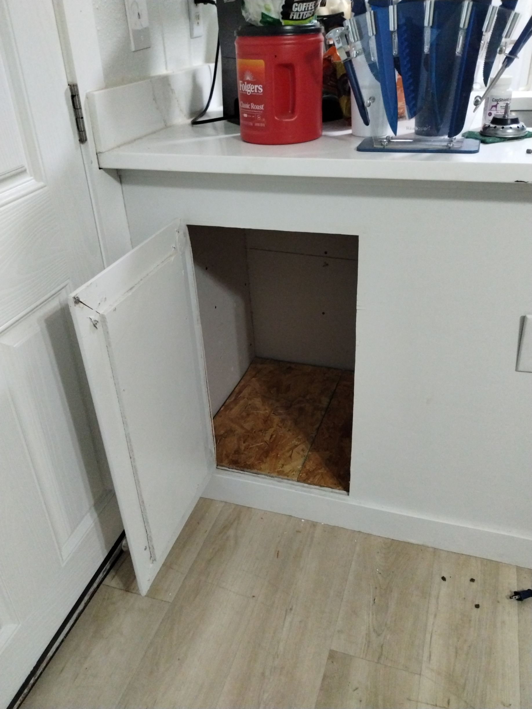 Open white cabinet door revealing a small, unfinished cubby under a countertop.
