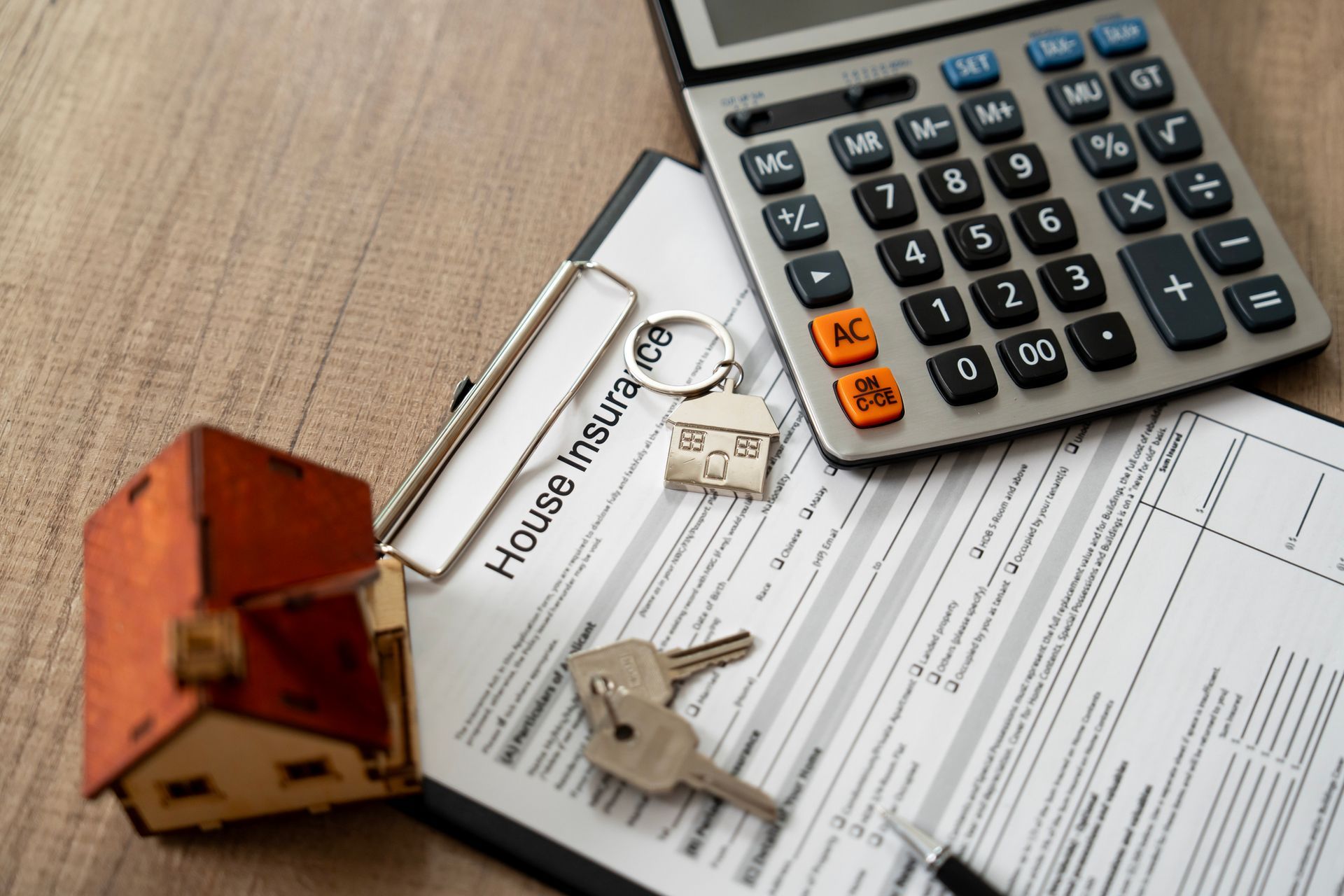 House insurance paperwork, a calculator, a toy house, and keys representing homeowners insurance. House insurance paperwork, a calculator, a toy house, and keys representing homeowners insurance.
