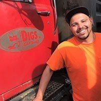 Man in orange shirt smiles next to a red truck with 