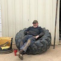 Man sitting in tire chair; gray shirt, jeans, and cap; metal wall background.