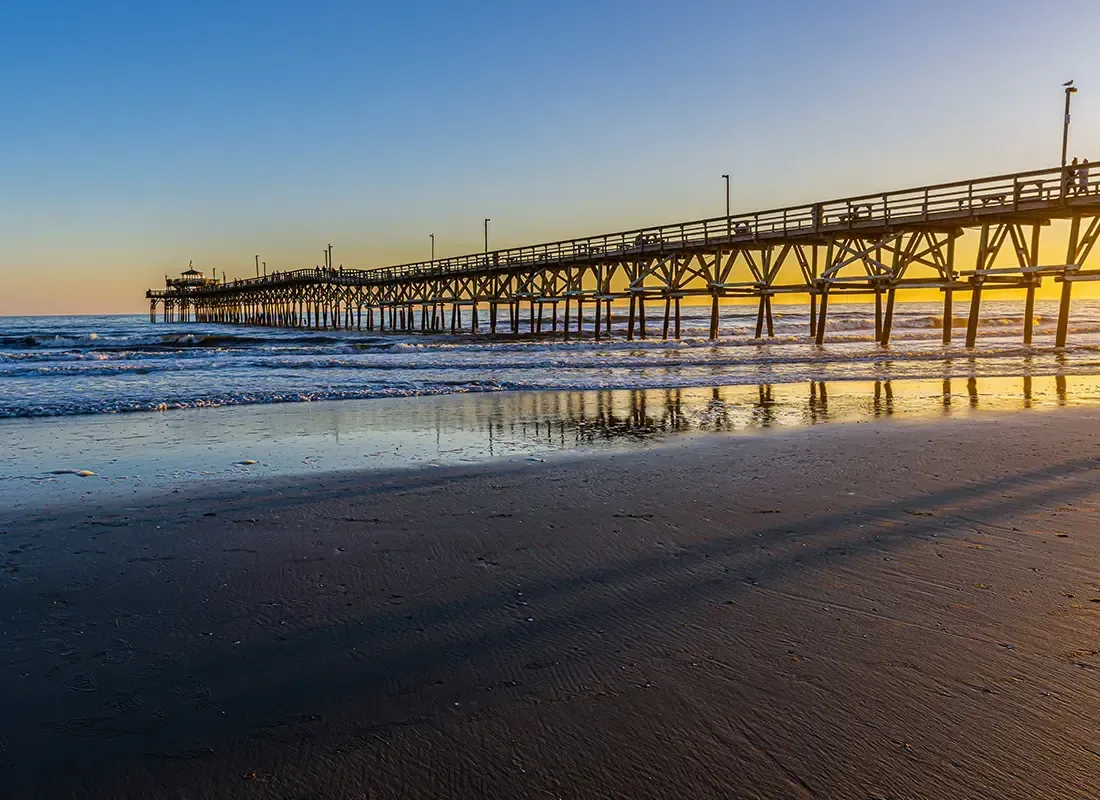 Sunset beach with a long pier stretching over calm water and wet sand