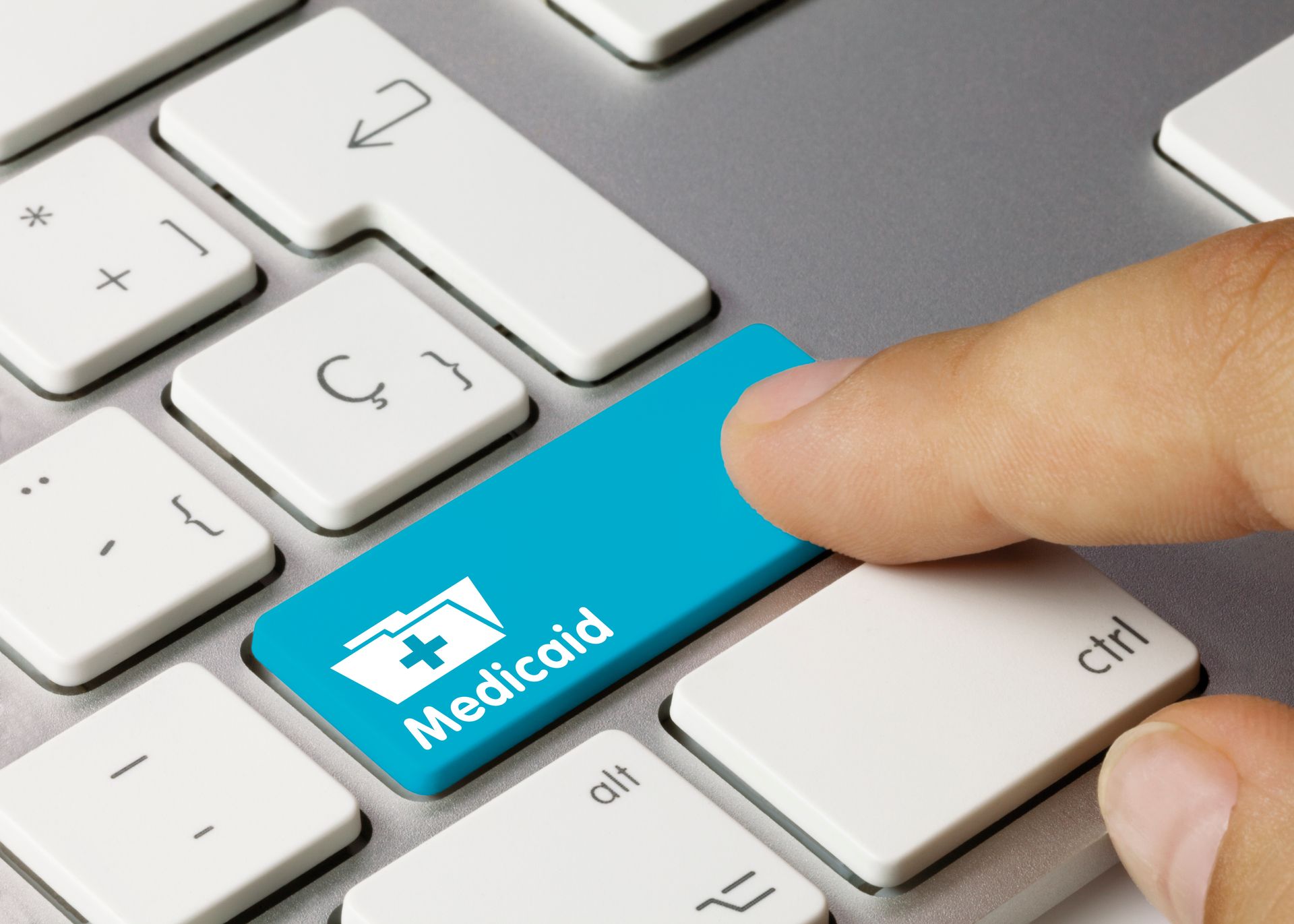 Hand inserting a blue Medicaid card into a white computer keyboard