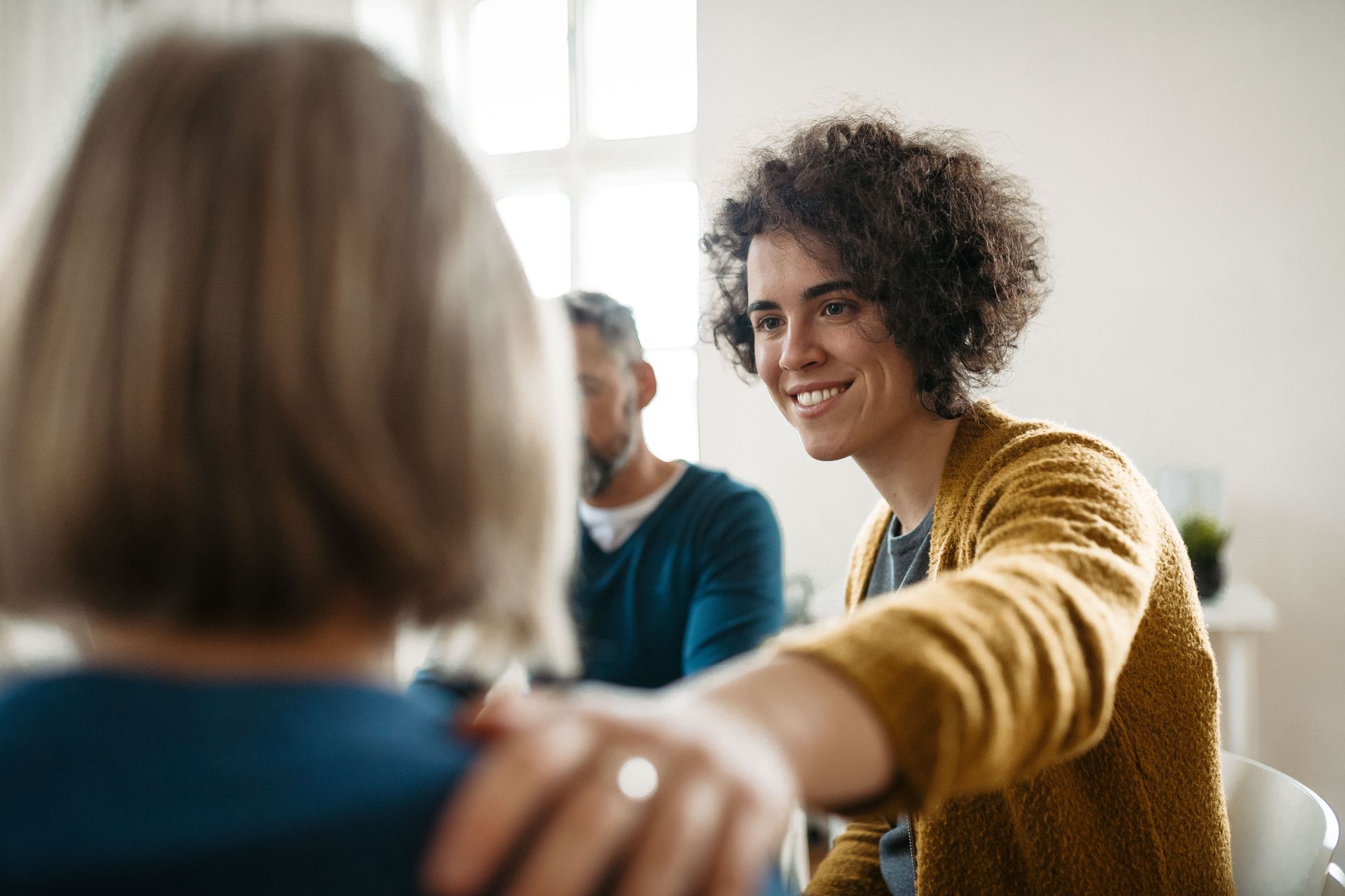 Smiling person in a yellow sweater reaching out in a bright meeting room