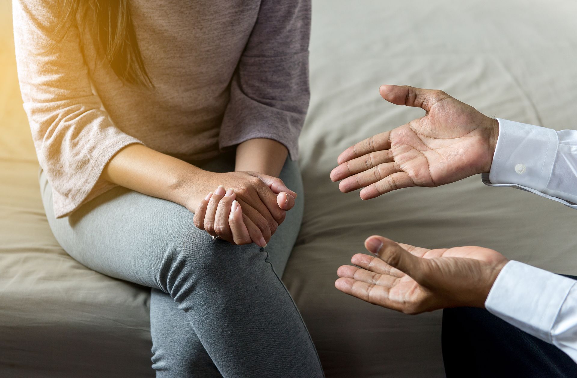 Two people seated in conversation, with one gesturing and the other sitting with hands clasped.