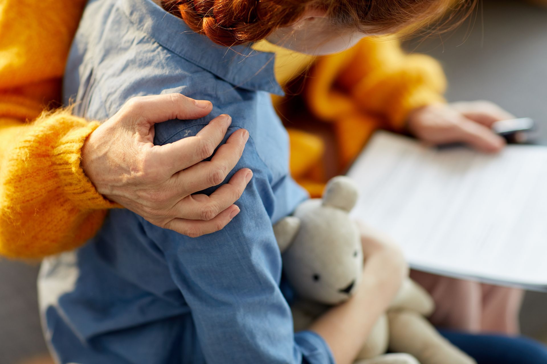 Adult holding a child in a blue outfit, with a stuffed rabbit and a notebook nearby