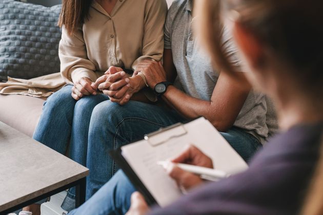 Counseling session with two seated people and a therapist taking notes on a clipboard