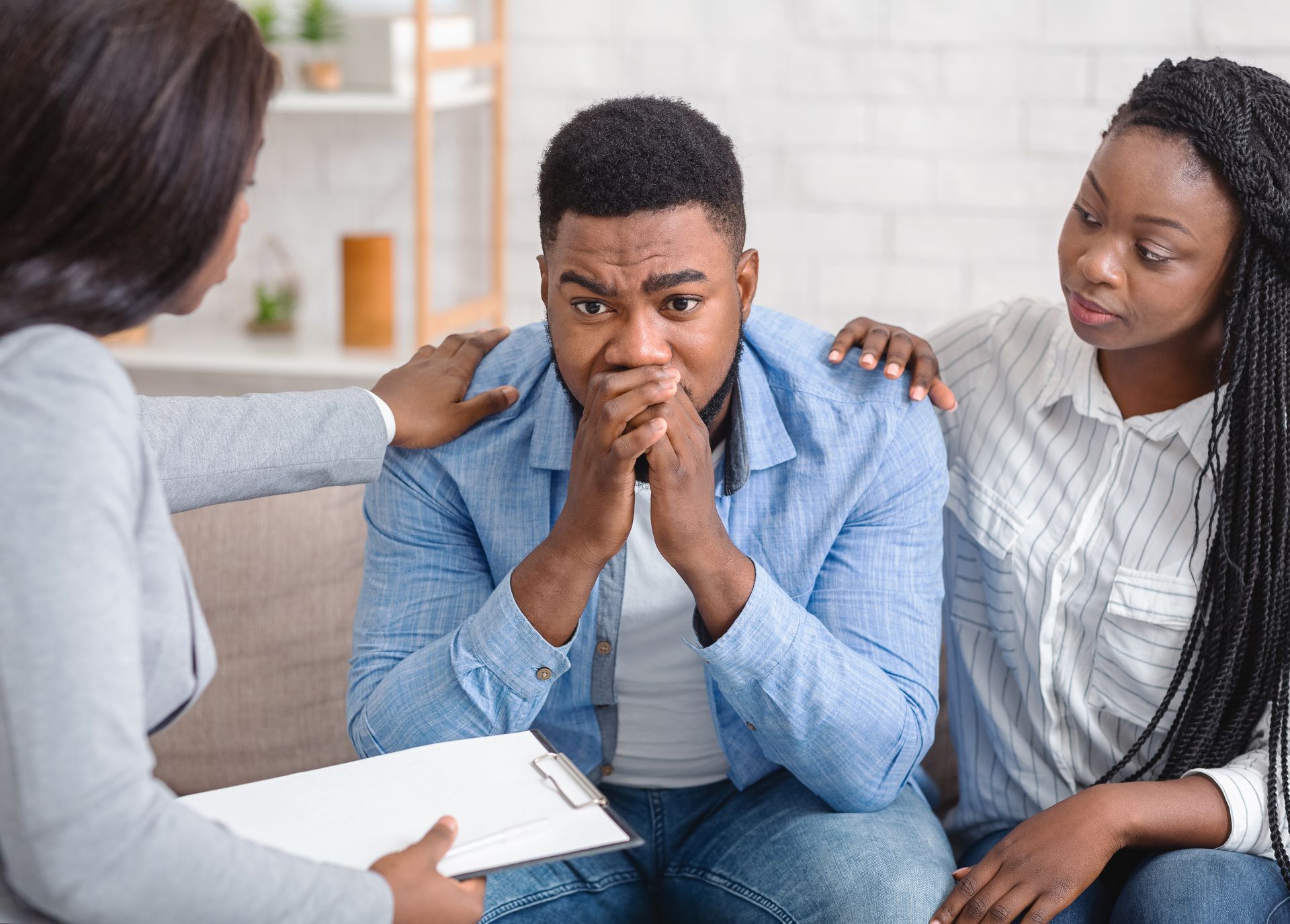 Three people in a counseling session, one man looking worried with two women listening supportively.