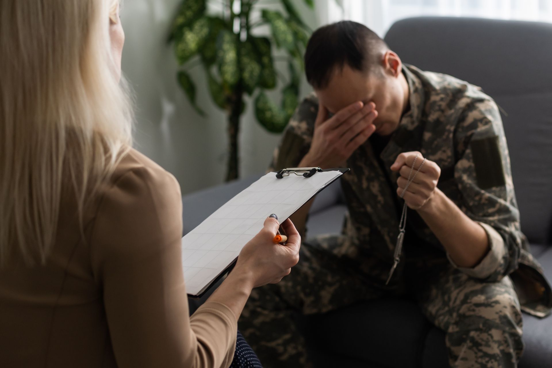 Counselor taking notes while a distressed man in camouflage sits on a couch with his head in his hands