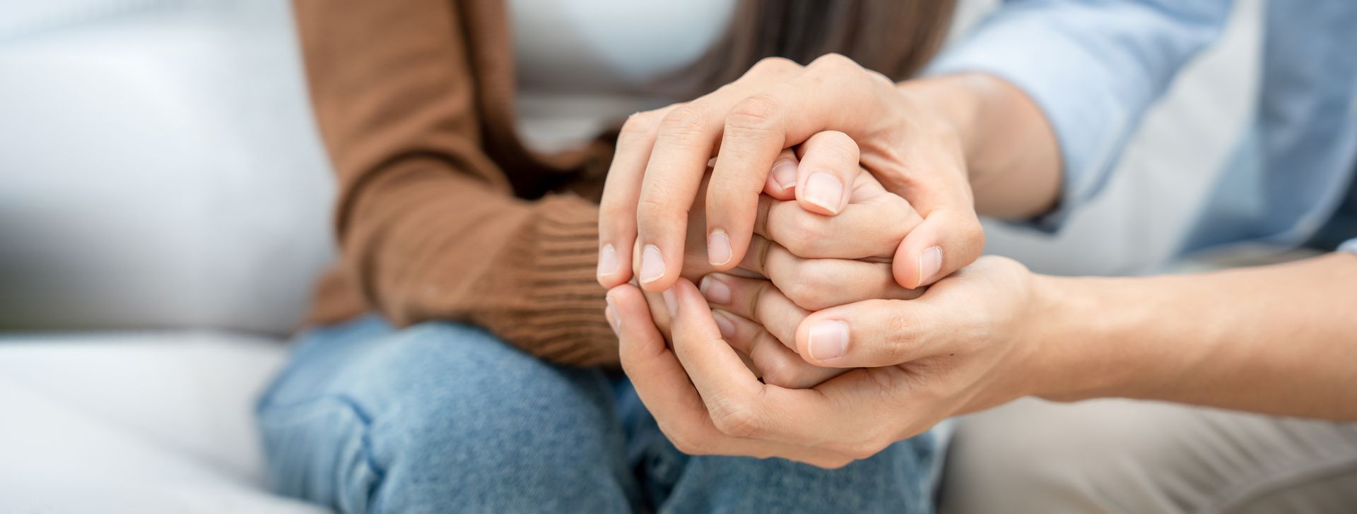 Two people holding hands on a couch, showing support and comfort