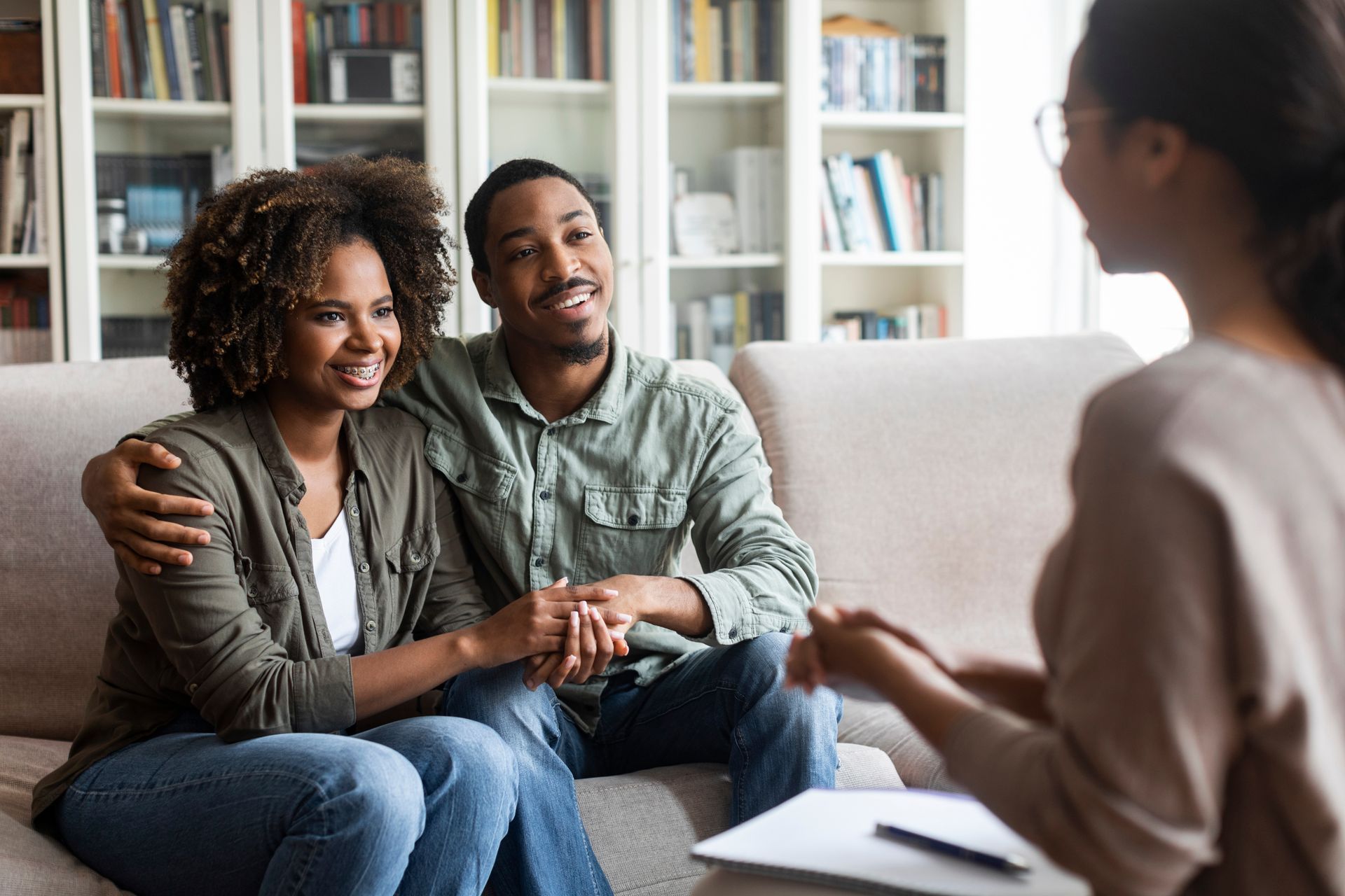 Two people sitting on a couch in a bright room, smiling during a conversation with a therapist.