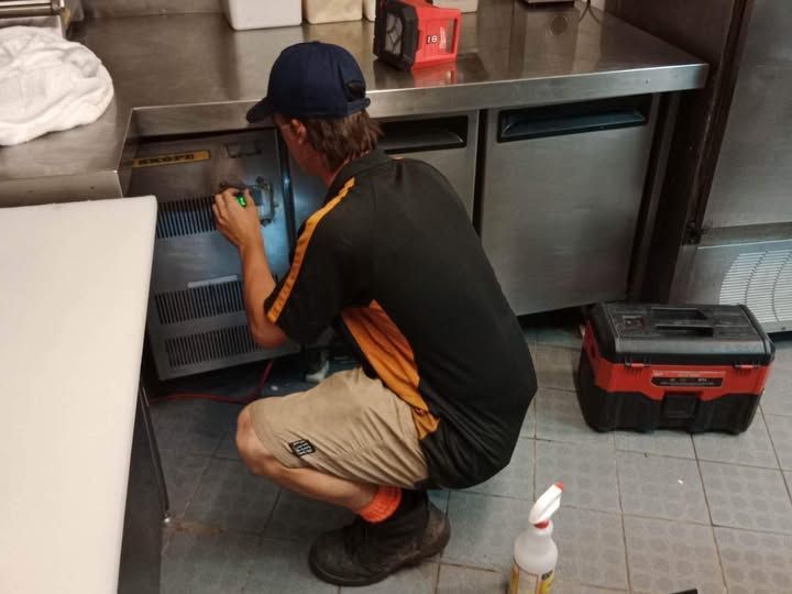 A Man Is Working on A Refrigerator in A Kitchen — Recharged Air & Electrical in Innisfail, QLD