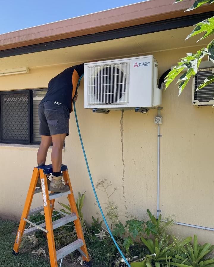 A Man Is Standing on A Ladder Next to An Air Conditioner — Recharged Air & Electrical in Smithfield, QLD