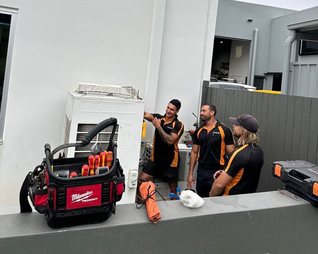 A Group of Men Are Working on An Air Conditioner Outside of A Building — Recharged Air & Electrical in Innisfail, QLD