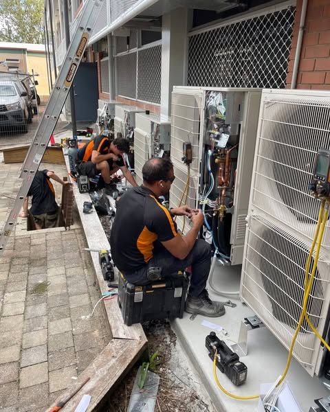 A Group of Men Are Working on An Air Conditioner Outside of A Building — Recharged Air & Electrical in Innisfail, QLD