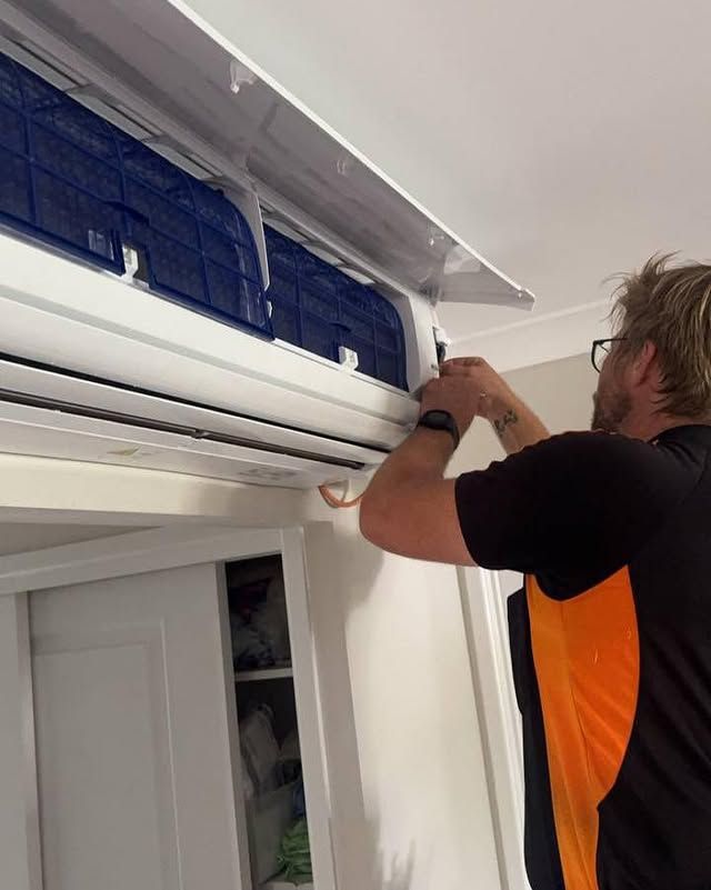 A Man Is Working on An Air Conditioner in A Room — Recharged Air & Electrical in Innisfail, QLD