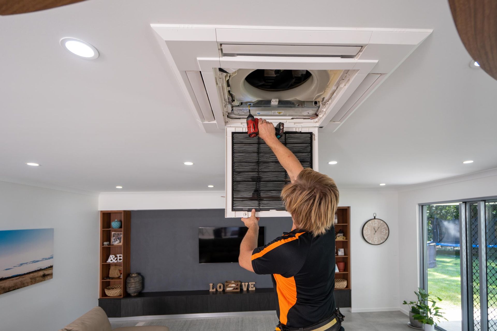 A Man Is Working on A Ceiling Fan in A Living Room — Recharged Air & Electrical in Innisfail, QLD