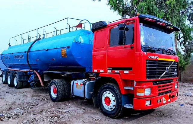 Camión cisterna rojo con un tanque cilíndrico azul estacionado en un camino de tierra.