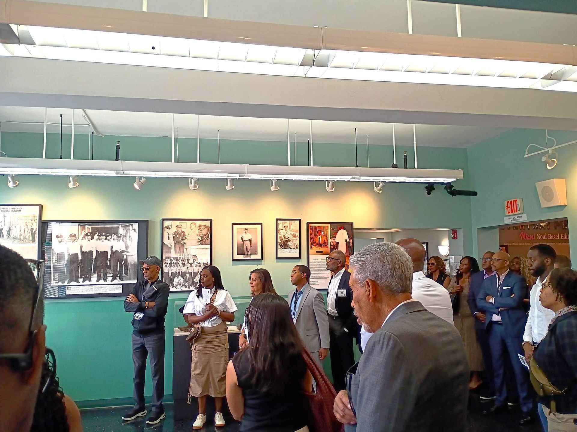 Visitors standing in a gallery, viewing framed artworks on teal walls