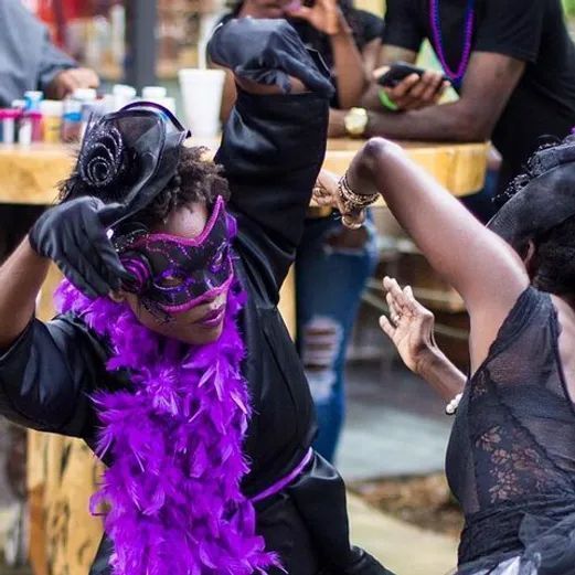 Masked dancers in black and purple costumes performing at a lively outdoor event