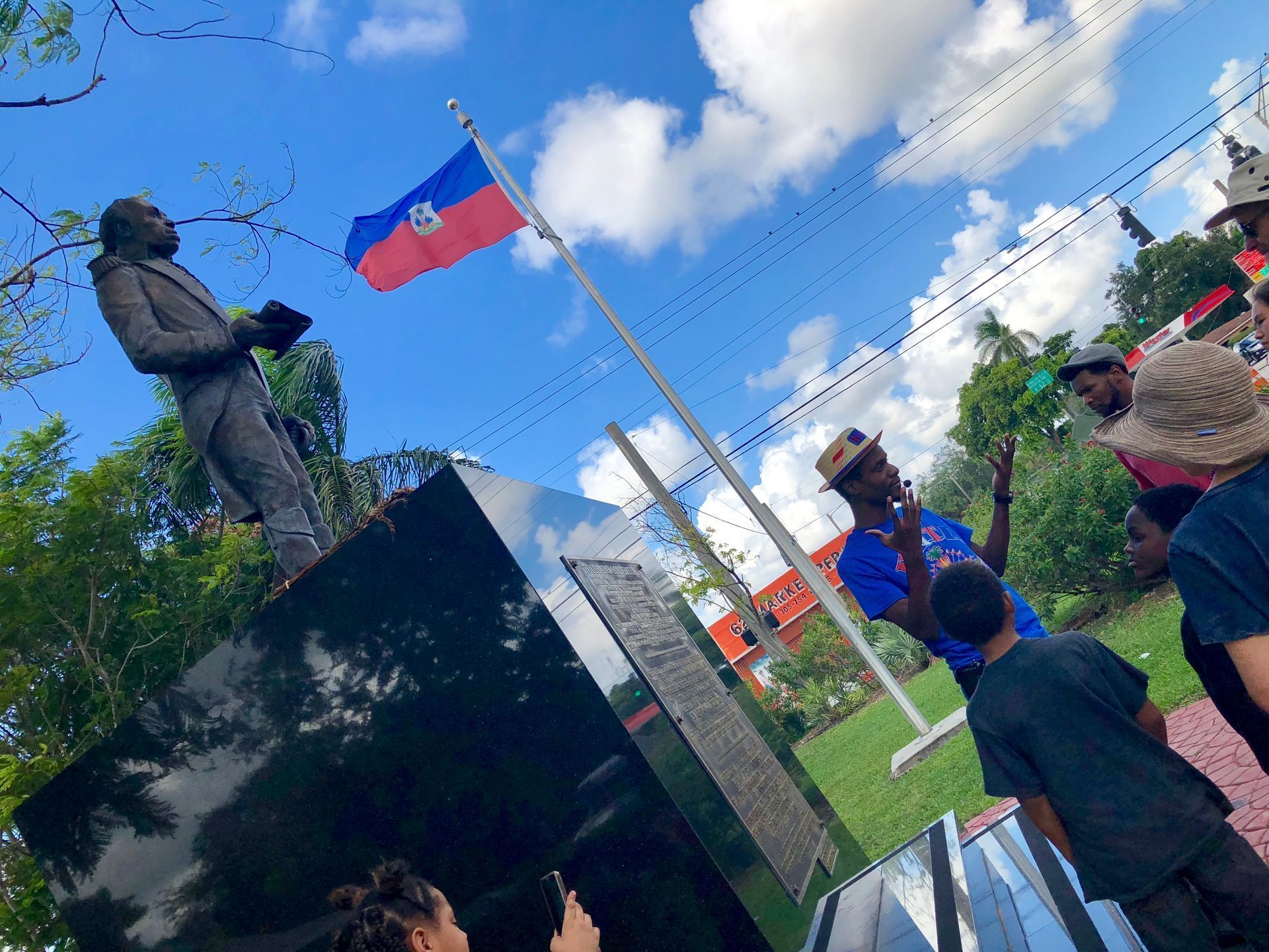 People standing by a bronze statue and a Taiwanese flag under a bright blue sky
