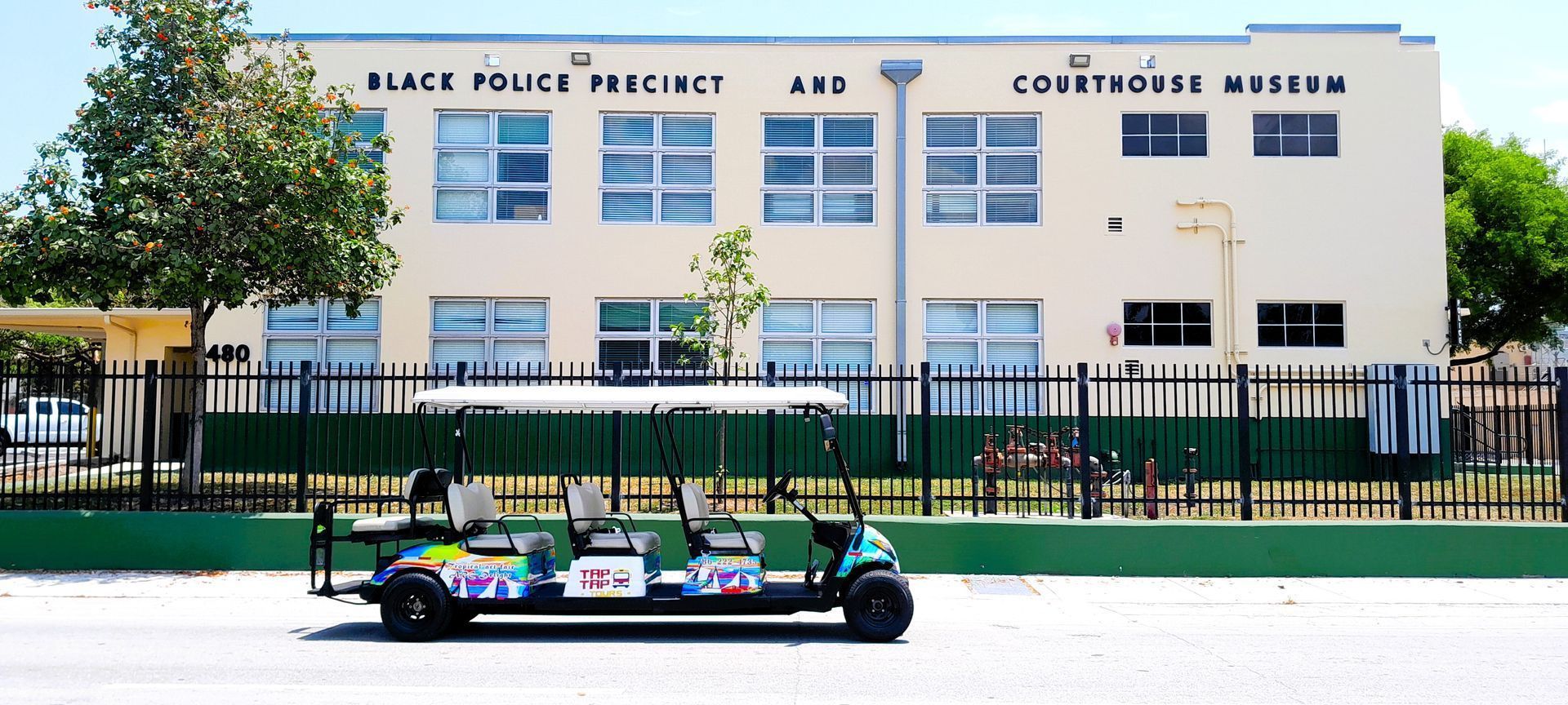 Formula race car on a track in front of a police district building with a fence and trees