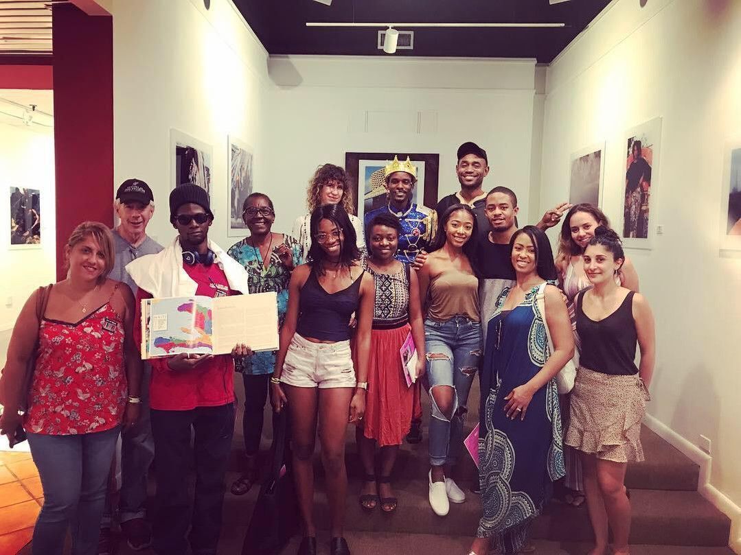 Group of people posing in a hallway, smiling and holding a framed sign.