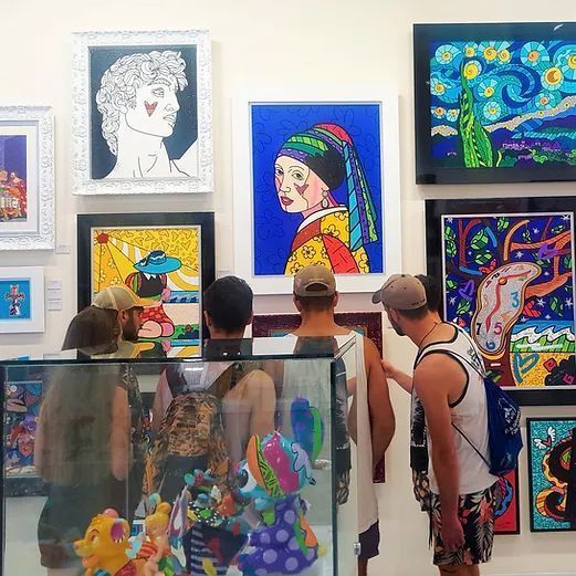 Visitors view colorful pop art paintings in a gallery with glass display cases in the foreground