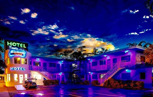 Neon-lit hotel at dusk with a glowing purple facade and colorful sunset sky