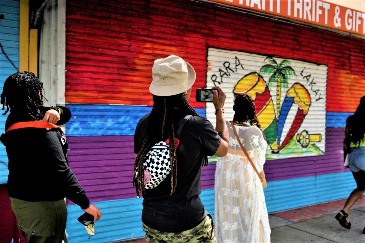 People painting a colorful mural on a shuttered storefront with a rainbow and palm tree design