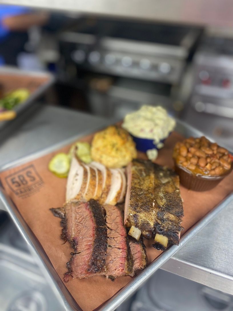 A wooden cutting board with meat and beans on it