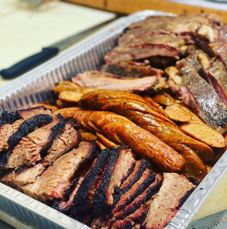 A tray of meat and sausages is sitting on a table.