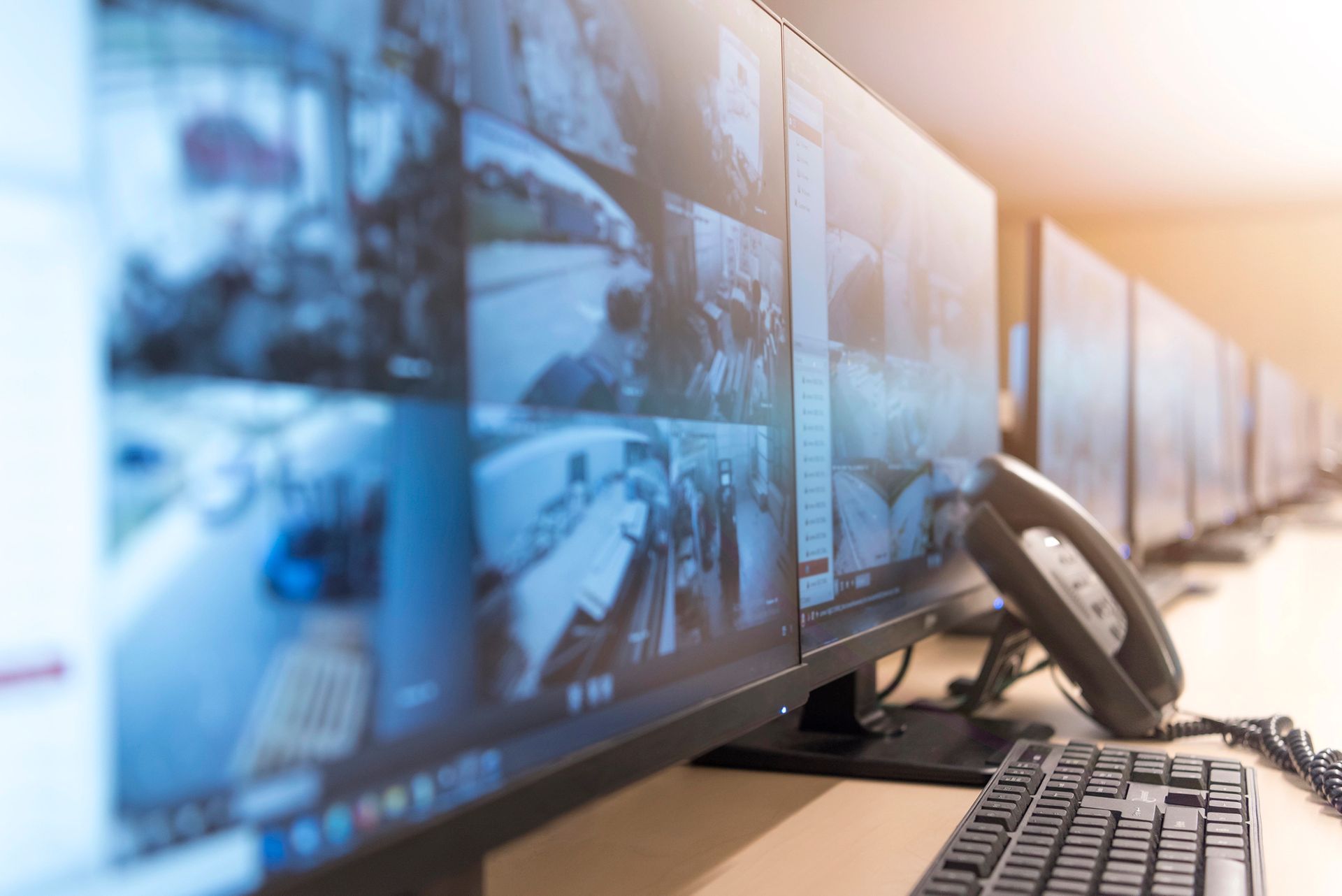 Una fila di monitor di sicurezza che mostrano filmati di sorveglianza accanto a un telefono fisso e una tastiera.
