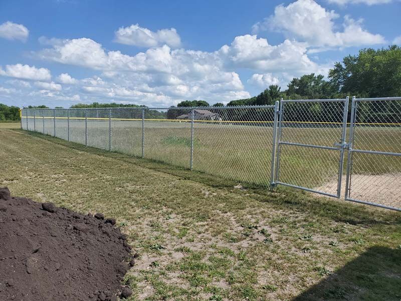 Chain-link fence along a grassy field under a blue, partly cloudy sky