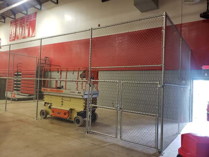 Chain-link enclosure with a yellow scissor lift inside a red-and-gray warehouse area