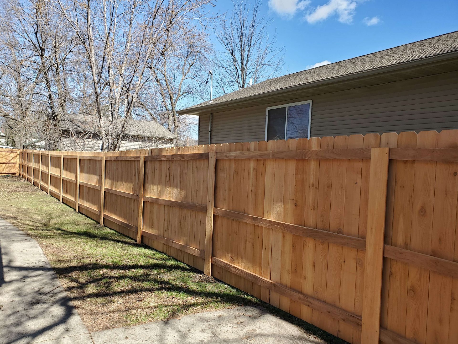 Long wooden privacy fence beside a tan house under a blue sky on a sunny day