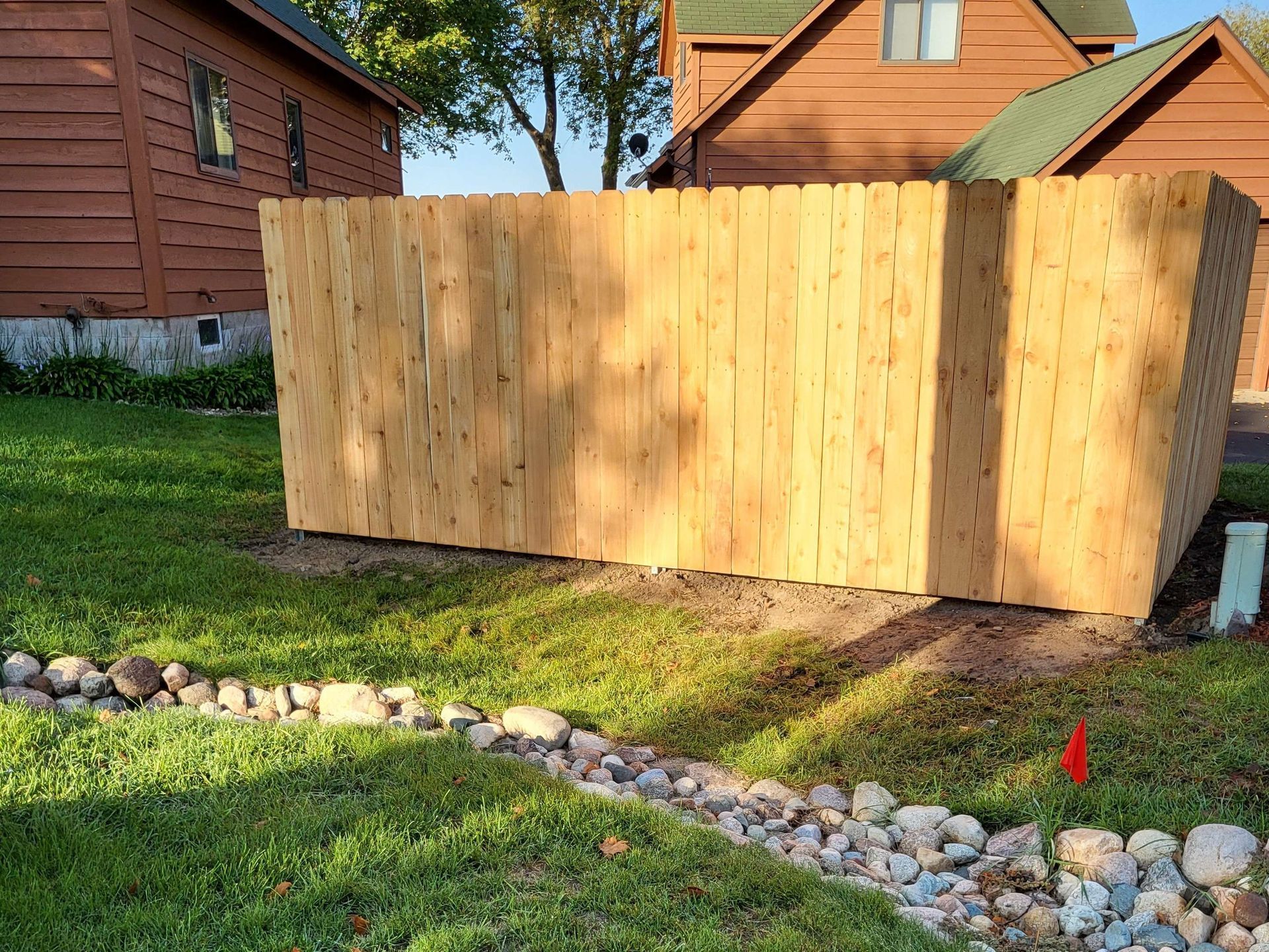 Wooden fence panels under construction in a backyard beside a stone border and grassy lawn
