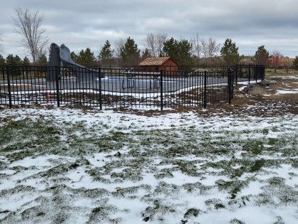 Snowy fenced yard with a small pavilion and bare trees in the background